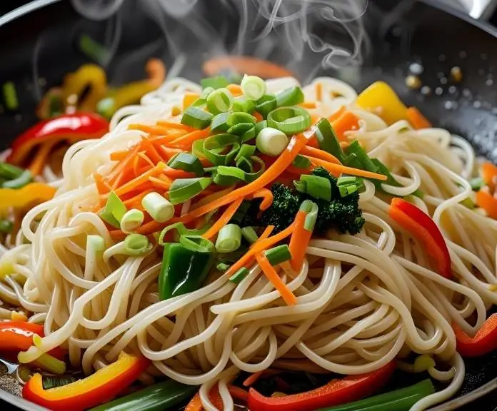 A steaming bowl of egg white noodle stir-fry with colorful bell peppers, snap peas, shredded carrots, and green onions that was just made.