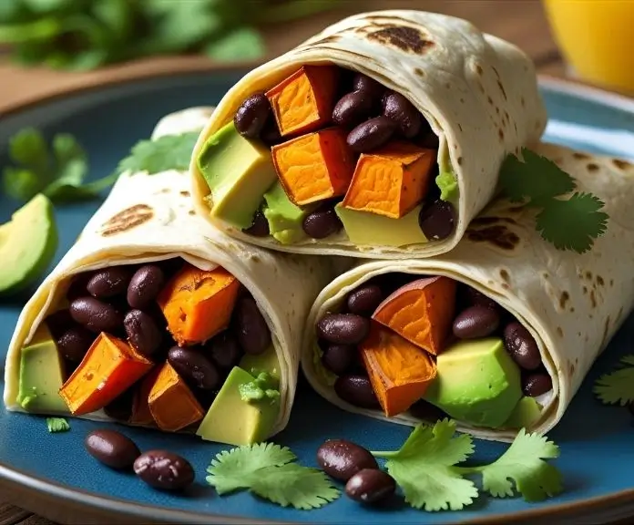 A close-up of a sliced breakfast burrito with sweet potatoes, black beans, and avocado inside. The vegetables are bright and the avocado is creamy.