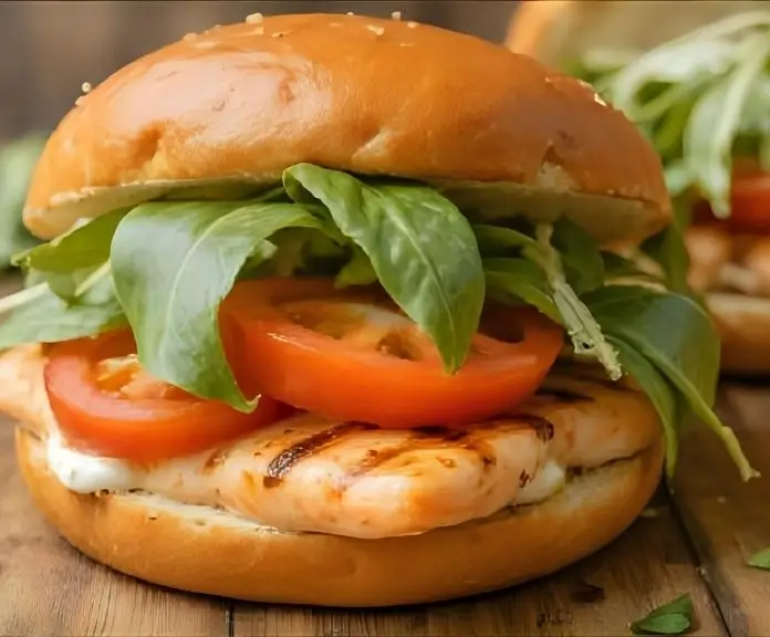 A toasted brioche bread sandwich with grilled salmon, lemon-herb mayo, arugula, and tomato.