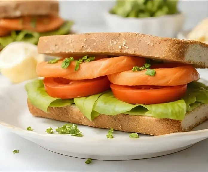 A healthy salmon sandwich with grilled salmon, avocado spread, lettuce, and tomato on whole grain bread.