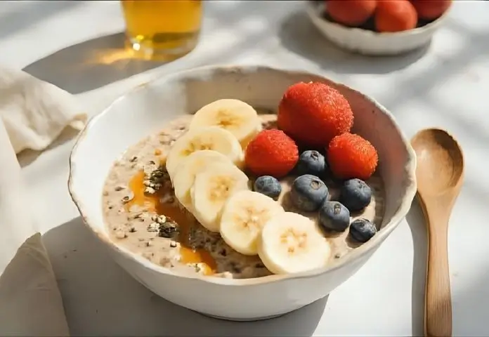 A close-up of a colorful protein oatmeal bowl with mixed berries, chia seeds, banana slices, and a drizzle of honey on top.