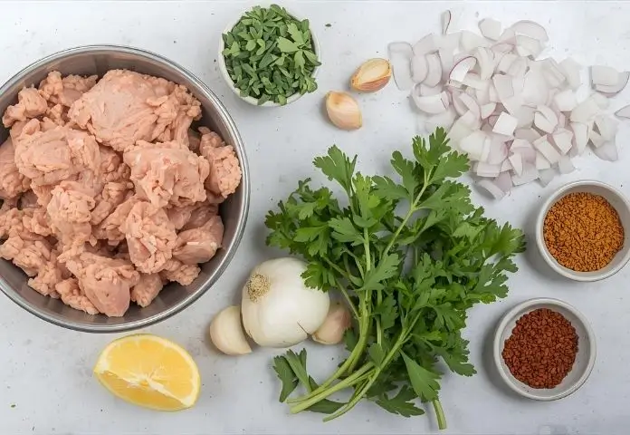 Flat lay of core ingredients for ground chicken recipes including fresh ground chicken, diced onions, garlic cloves, fresh herbs, and assorted spices displayed on a neutral background.