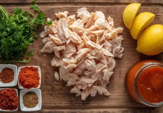 Fresh herbs, citrus wedges, bowls of spice blends, and jars of marinades displayed together as flavor boosters for shredded chicken.